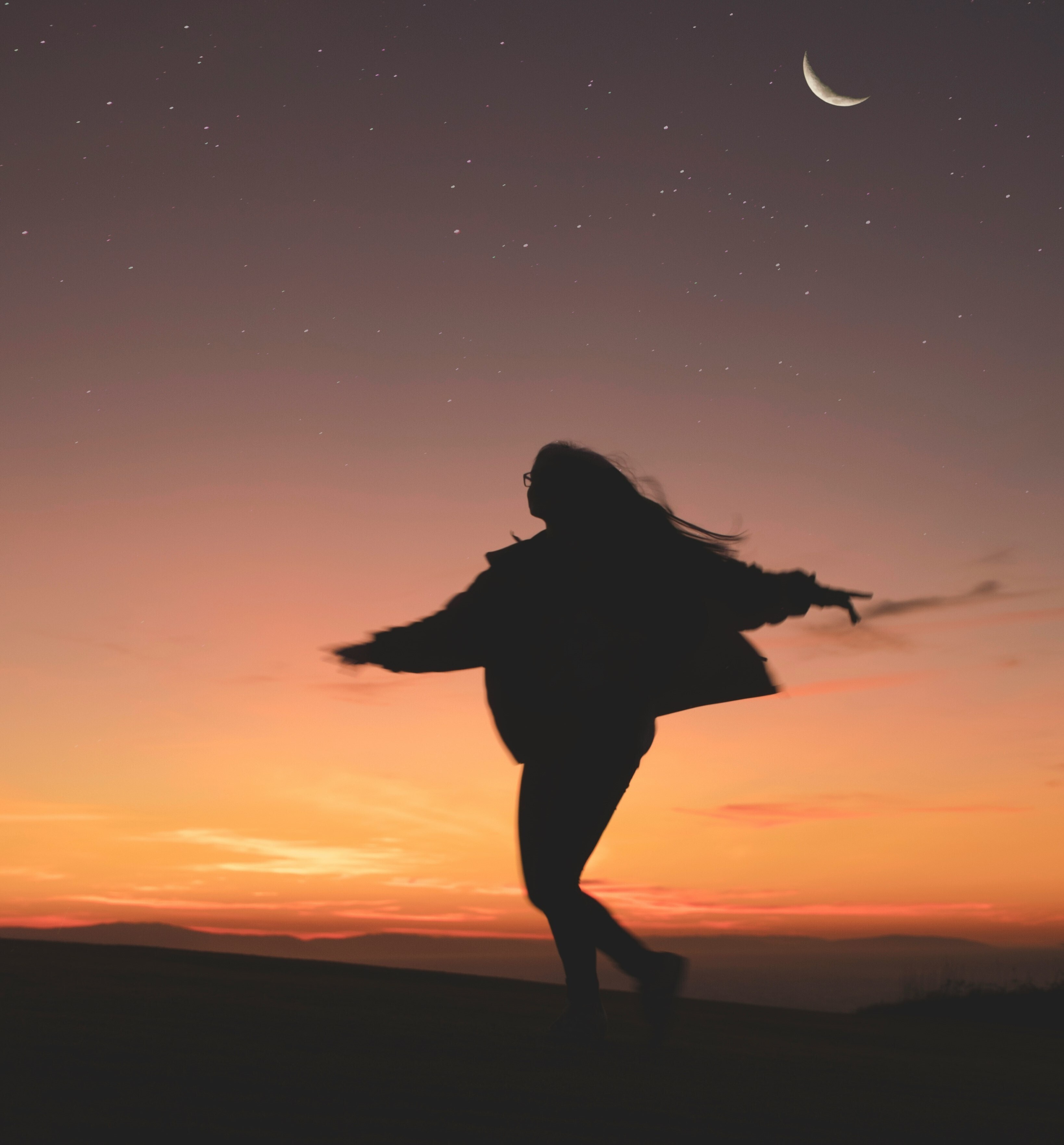 Woman's silhouette as she pretends to fly, against a red sunset