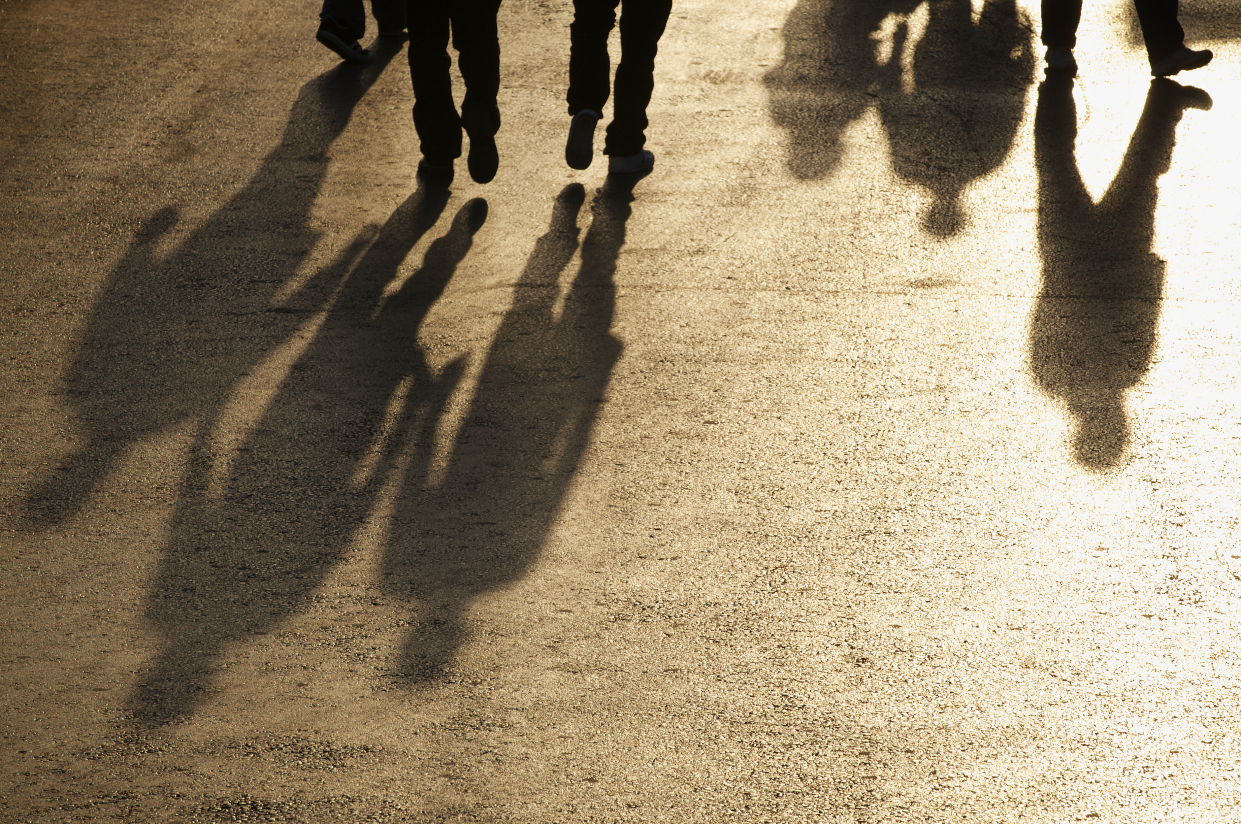 Shadows of businessman walk together on wide street shining the golden light of reflected sun